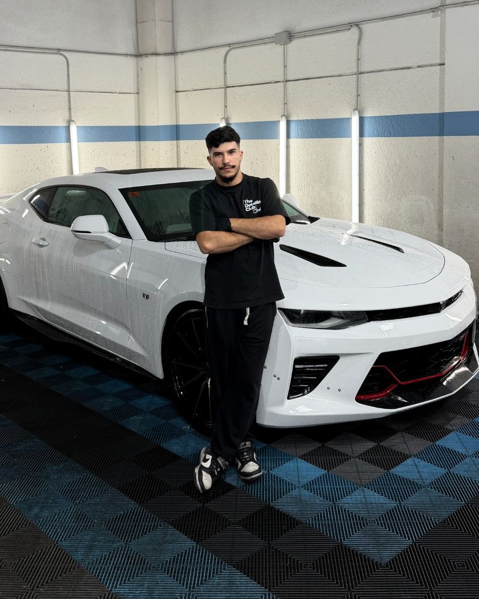 Mario, de brazos cruzados, junto a un Chevrolet Camaro blanco en su taller